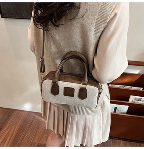 Detail of a brown leather and woven Boston bag worn by a model in a cozy interior