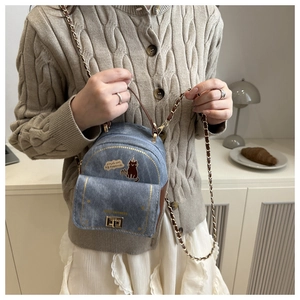 Detail of mini denim crossbody bag featuring cartoon cat illustration and metal chain strap