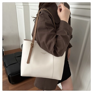 Close-up of beige tote bag with brown leather straps and gold buckle detail on a coat