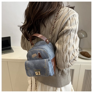 Mini denim backpack with cat print and chain strap worn over a beige knitted sweater