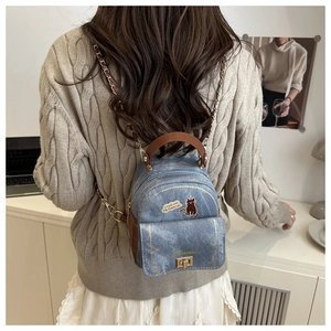 Mini denim backpack with cat print and metal chain strap shown on a model's back