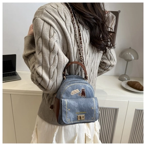 Detail of denim mini backpack with cat print and leather straps shown on a model
