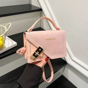 Pink matte crossbody handbag with gold clasp and chain, held against minimalist stairs