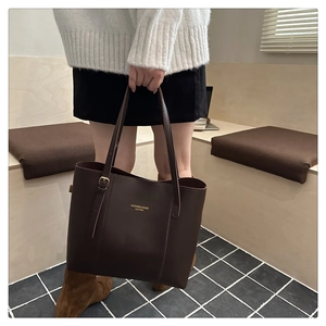 Detailed close-up of dark brown leather tote bag with gold lettering and hardware buckle
