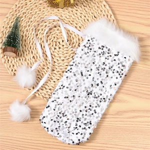 Detail of white sequined Christmas wine bottle cover with plush trim and pom-pom drawstrings