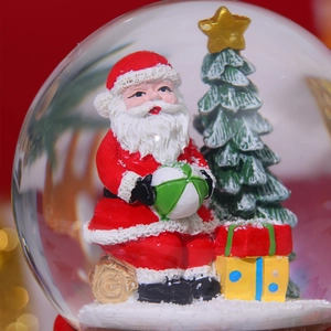 Close-up of a festive snow globe featuring Santa Claus and a Christmas tree on a red background