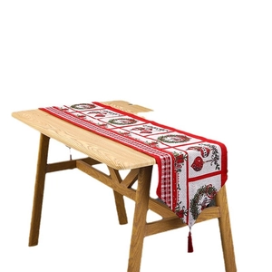 Christmas table runner with festive wreath patterns and red tassels on wooden table