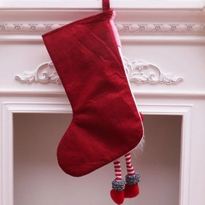 Chaussette de Noël rouge en peluche avec jambes rayées sur une cheminée blanche