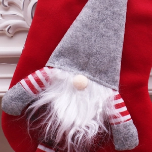 Détail d'une chaussette de Noël rouge ornée d'un gnome gris en peluche avec une barbe blanche