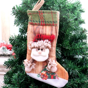 Detail of Christmas stocking featuring 3D Santa plush and festive plaid cuff on a tree
