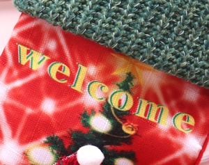 Detail of red Christmas stocking featuring festive tree print and yellow Welcome text