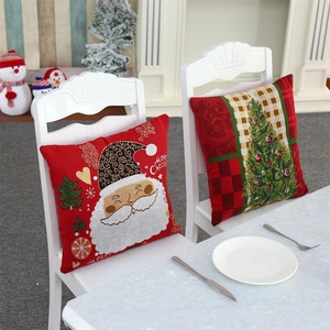 Detail of red Merry Christmas pillow cases with Santa embroidery on a white wooden chair