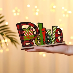 Hand holding a wooden Believe Christmas letter sign with festive plaid patterns and gift box
