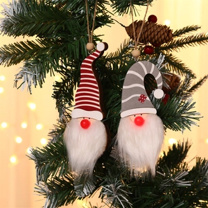 Detail of glowing Christmas tree gnome pendants with striped hats hanging on pine branches