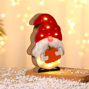 Close-up of wooden glowing gnome with orange pumpkin and LED lights on snow base