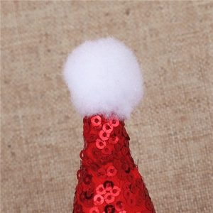Dettaglio macro di un mini cappello di Babbo Natale con paillettes rosse e pompon bianco