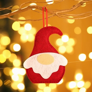 Red and white felt Christmas gnome ornament hanging on a golden branch with bokeh lights