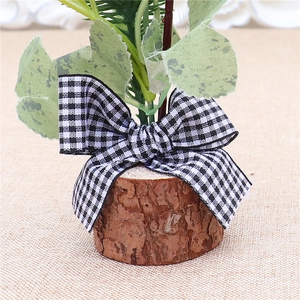 Close-up of a mini Christmas tree with a rustic wood base and black-white checkered bow