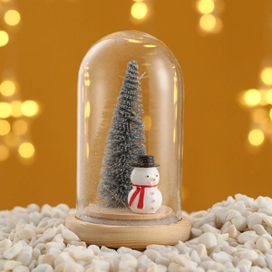 Close-up of a miniature Christmas tree and snowman inside a glass dome with a wood base