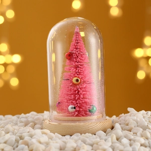 Close-up of pink mini Christmas tree in glass dome with wood base and bokeh lights