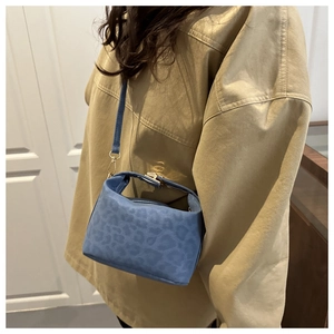 Détail d'un micro sac bandoulière bleu à motif léopard avec boucle dorée sur mannequin