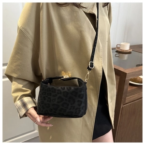 Détail d'un sac bandoulière léopard avec fermoir doré porté avec un trench-coat