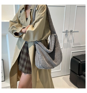 Detailed side view of large grey corduroy crossbody bag worn by a model in interior