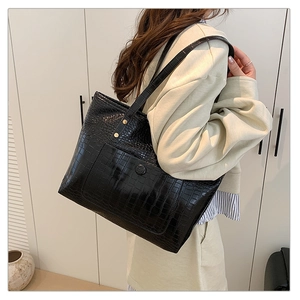 Detail of a large black crocodile pattern tote bag with front pocket and metal button