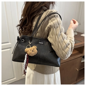 Detail of black wax leather tote bag with fashion label and bear pendant accessory