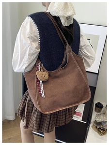 Close-up of brown suede hobo bag with teddy bear charm and striped ribbon detail