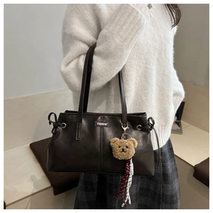 Detail of dark brown tote bag with metal label, teddy charm and striped rope accessory