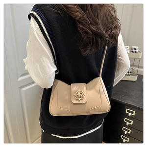 Detailed view of a beige leather underarm bag featuring an ornate gold buckle and slim strap