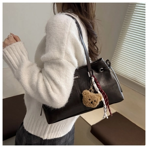 Detail view of large dark brown leather tote bag with cute bear charm and woven cord