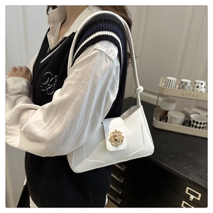 Detail of white baguette bag featuring a gold floral buckle and knotted shoulder strap
