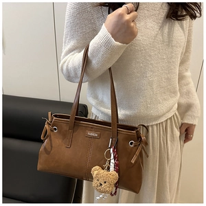 Detail of dark brown faux leather tote bag with FASHION label and plush bear charm