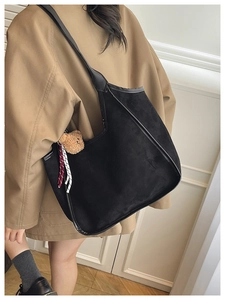 Detail of black suede shoulder bag featuring a cute plush bear charm and wide strap