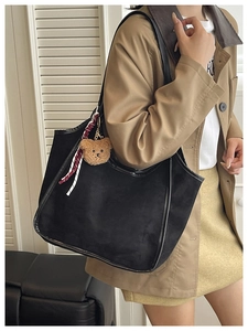 Detail of black suede tote bag with cute bear charm and checkered scarf accessory