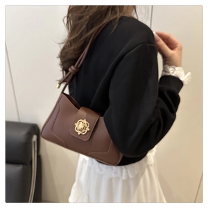 Detail of deep brown leather underarm bag with gold floral buckle on model shoulder