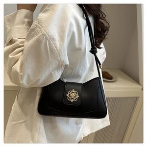 Primer plano de bolso de hombro negro con hebilla floral dorada y detalle de correa anudada