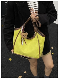 Detail view of yellow faux suede tote bag with brown trim and bear charm in outdoor setting