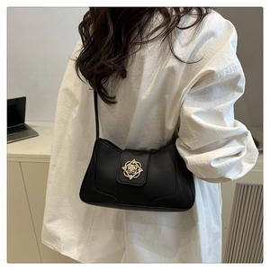 Bolso de hombro minimalista en cuero negro con hebilla floral dorada usado por una modelo