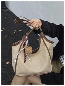 Close-up of beige suede bucket bag with contrast trim and cute brown plush bear charm