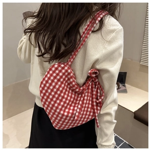 Detail of red gingham heart-shaped crossbody bag with bow accent on a model
