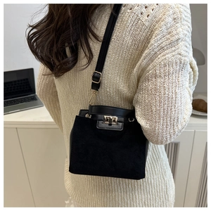 Detail of black suede crossbody bag with gold turn-lock closure on beige knit sweater