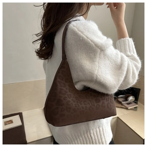 Detail of leopard print shoulder bag in dark brown suede finish worn by model