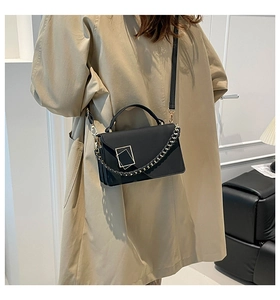 Detail of black leather handbag featuring dual gold square buckles and chain strap