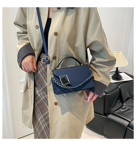 Detail of navy blue leather handbag with metallic buckle on a model in beige coat