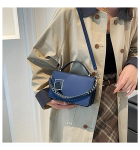 Close-up of navy blue crossbody bag featuring gold geometric hardware and woven chain strap