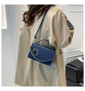 Detail of dark blue leather handbag with gold geometric buckle and metallic chain strap