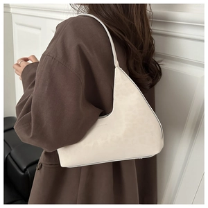 Minimalist cream leather underarm bag worn with a brown blazer on model shoulder